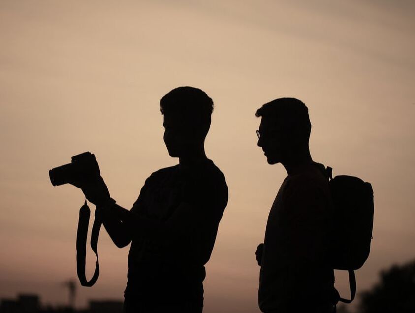 Two men sihouetted, one is holding a camera and showing the other how to use it